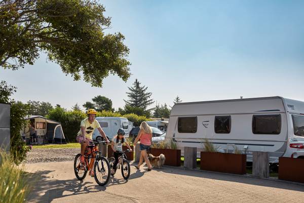A family is riding bicycles near their camper vans at Henne Strand Resort.