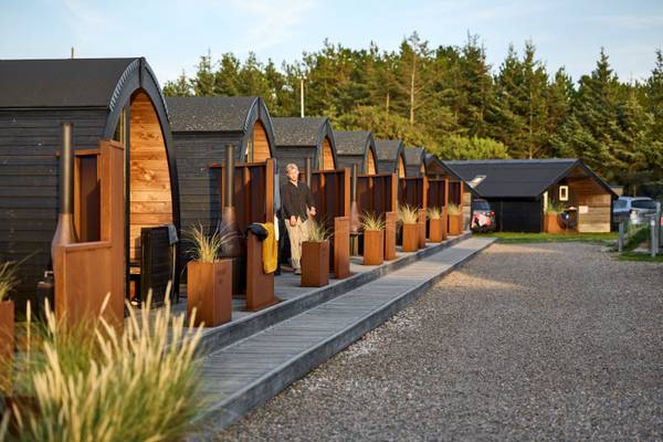 A row of wooden huts at Henne Strand Resort with a man standing in front.