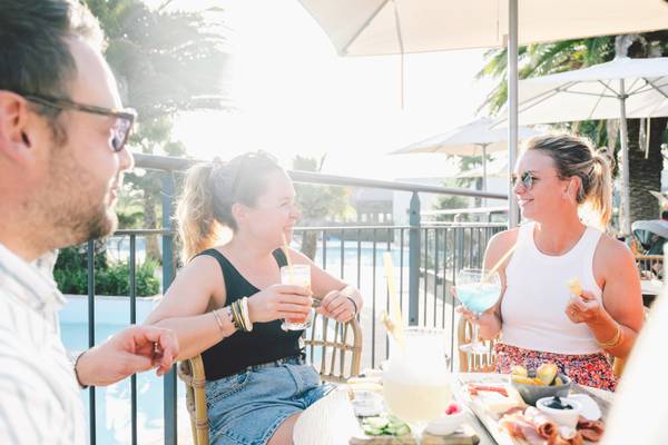 Tres personas sentadas junto a una piscina en un camping, dos mujeres sonriendo y un hombre hablando