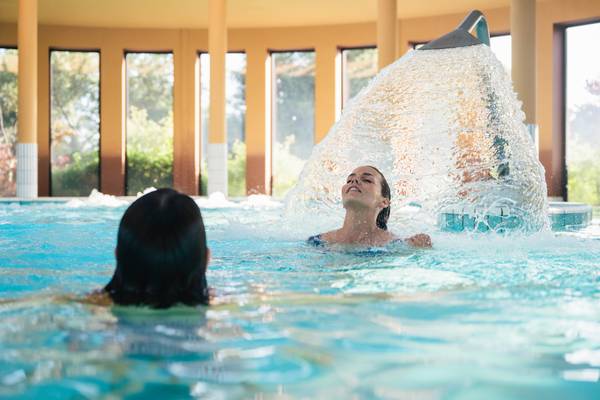 Dos mujeres nadando en una piscina cubierta con cascada en el Camping Les Mouettes