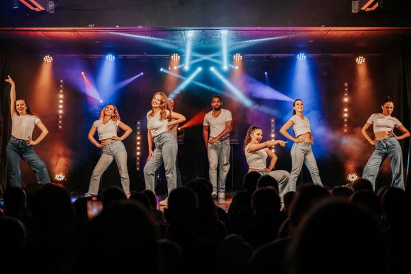 Un grupo de personas bailando en un escenario con luces de colores detrás de ellas.