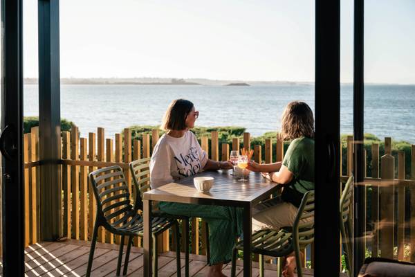 Dos mujeres disfrutando de bebidas en un balcón con vista al océano en Camping Les Mouettes.