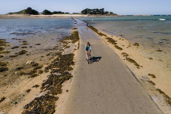 Una mujer montando una bicicleta en un camino cerca de la playa en Camping Les Mouettes.