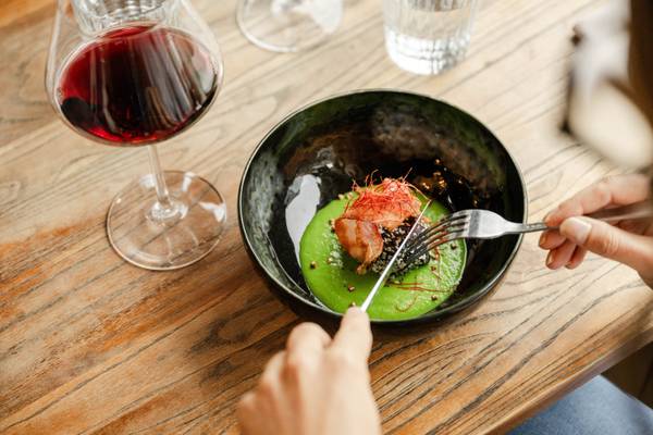 Una persona come un plato verde con tenedor y cuchillo sobre una mesa de madera.