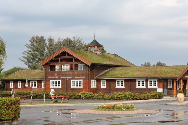 Eksternt af Jambo Feriepark med træbygning, grønt tag og udendørs picnicborde.
