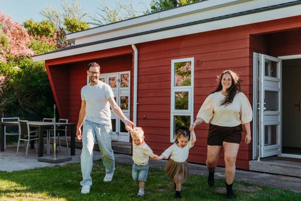 Eine vierköpfige Familie steht vor einem roten Haus, lächelt und hält Händchen.