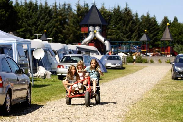 Tres niñas montan en un carrito rojo en el camino de grava del camping Jambo Feriepark.