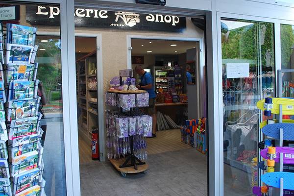 Entrada a la tienda del camping Nature Parc L`Ardéchois con productos en exhibición y un hombre dentro.