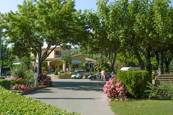 Entrada del camping Nature Parc L`Ardéchois con coches aparcados y personas caminando.