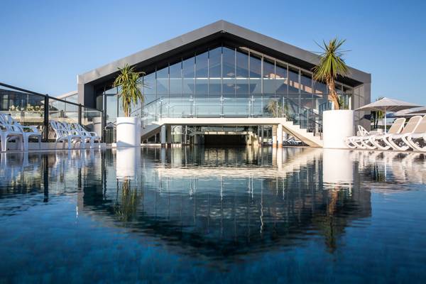 Un bâtiment moderne avec des murs en verre près d'une grande piscine au Camping Le Pin Parasol.
