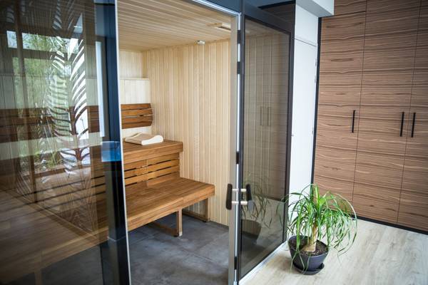 Vue intérieure d'un sauna avec un banc en bois et une porte en verre ouverte.