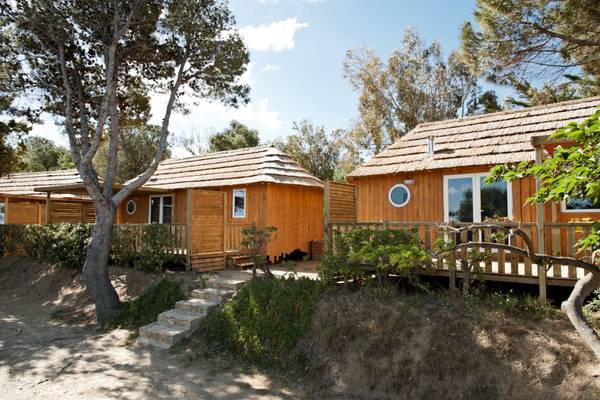 Zwei Holzhütten im Camping Les Criques de Porteils mit Strohdächern und Holzdecks.