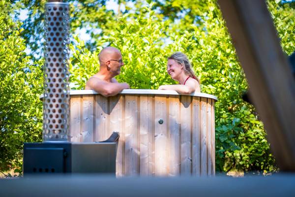 Una coppia si rilassa in un sauna in barile di legno con alberi sullo sfondo.
