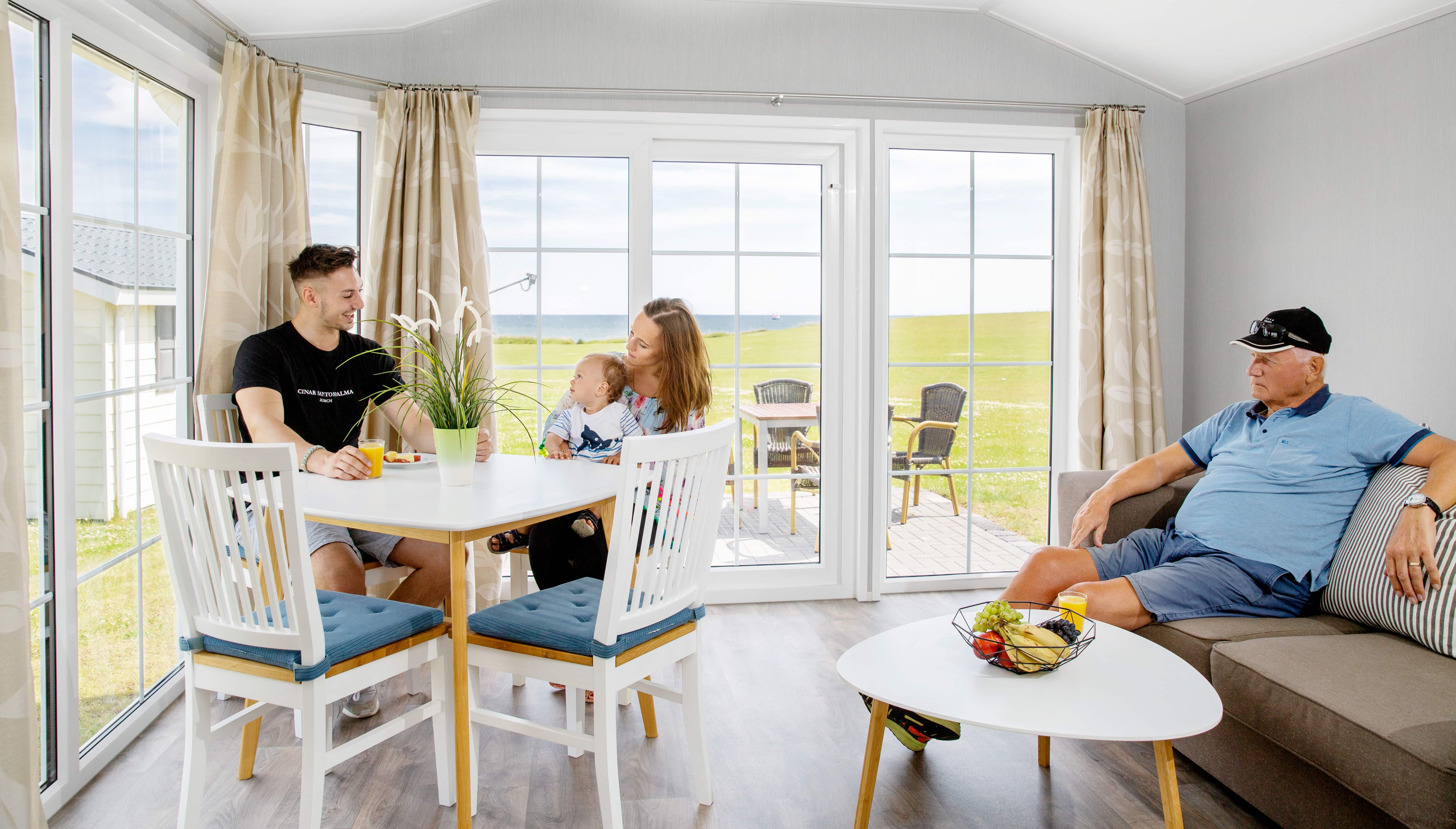 Familie sidder ved et bord i en campingplads med udsigt til havet.