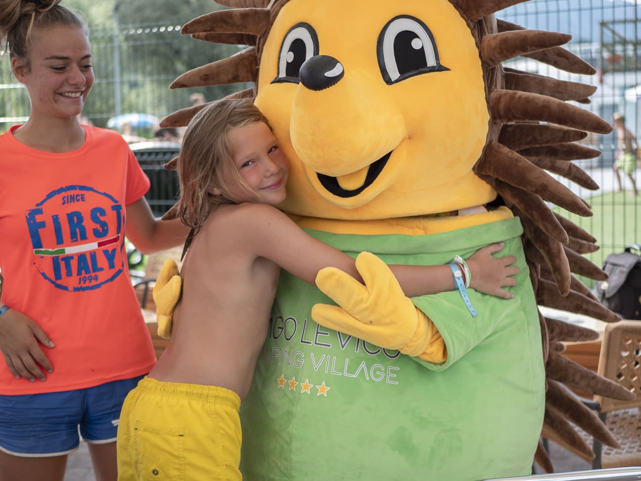 Una bambina abbraccia un grande mascotte al villaggio campeggio di Lago Levico.