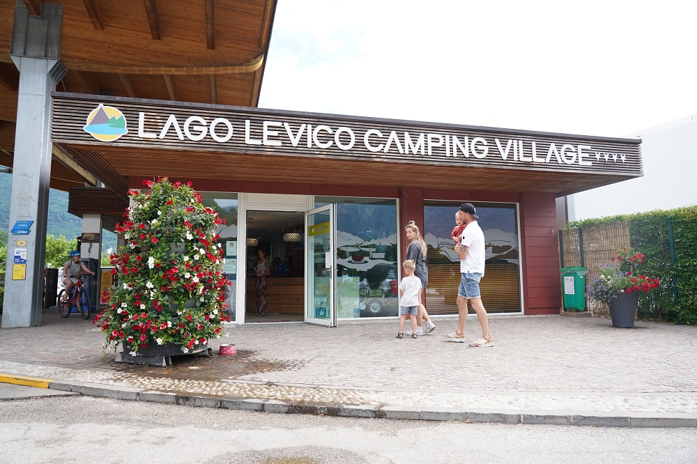 Ingresso del Camping Lago Levico con una famiglia che cammina verso l'ingresso.