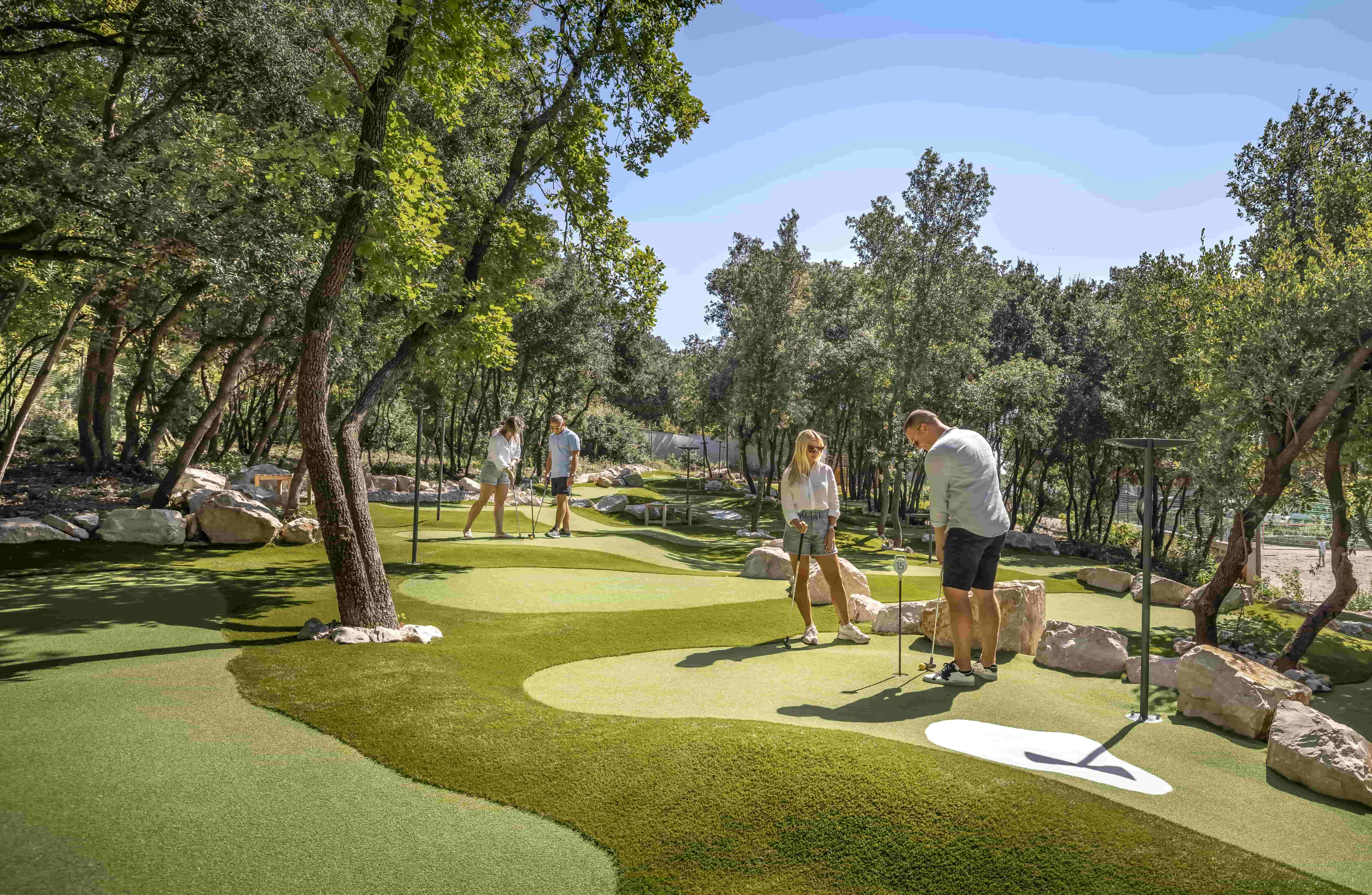 People playing golf on a green course at Camping Vestar with trees around