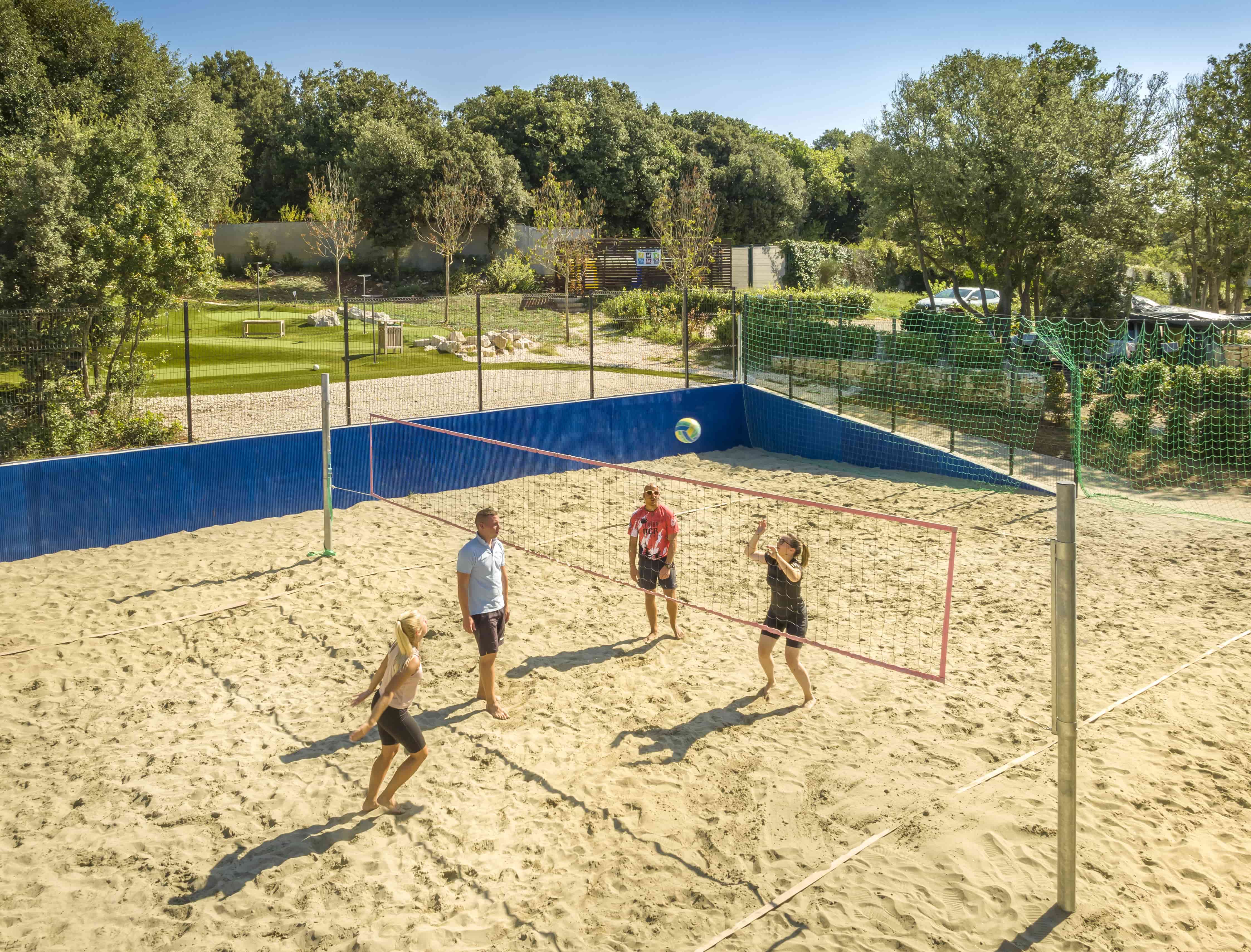 Four people playing volleyball on a sandy court at Camping Vestar.