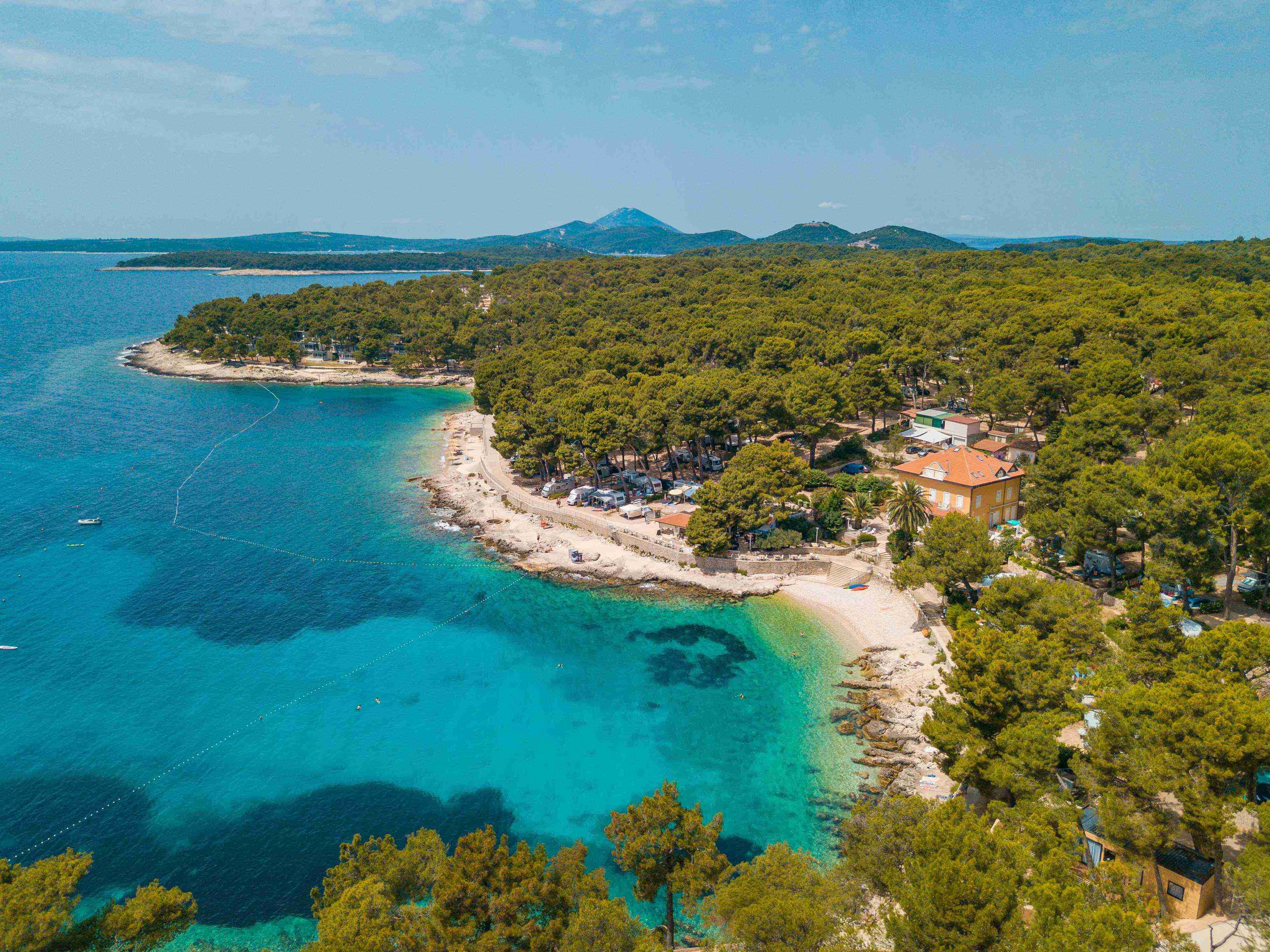 Aerial view of Camping Cikat with a beach, trees, and mountains in the background.