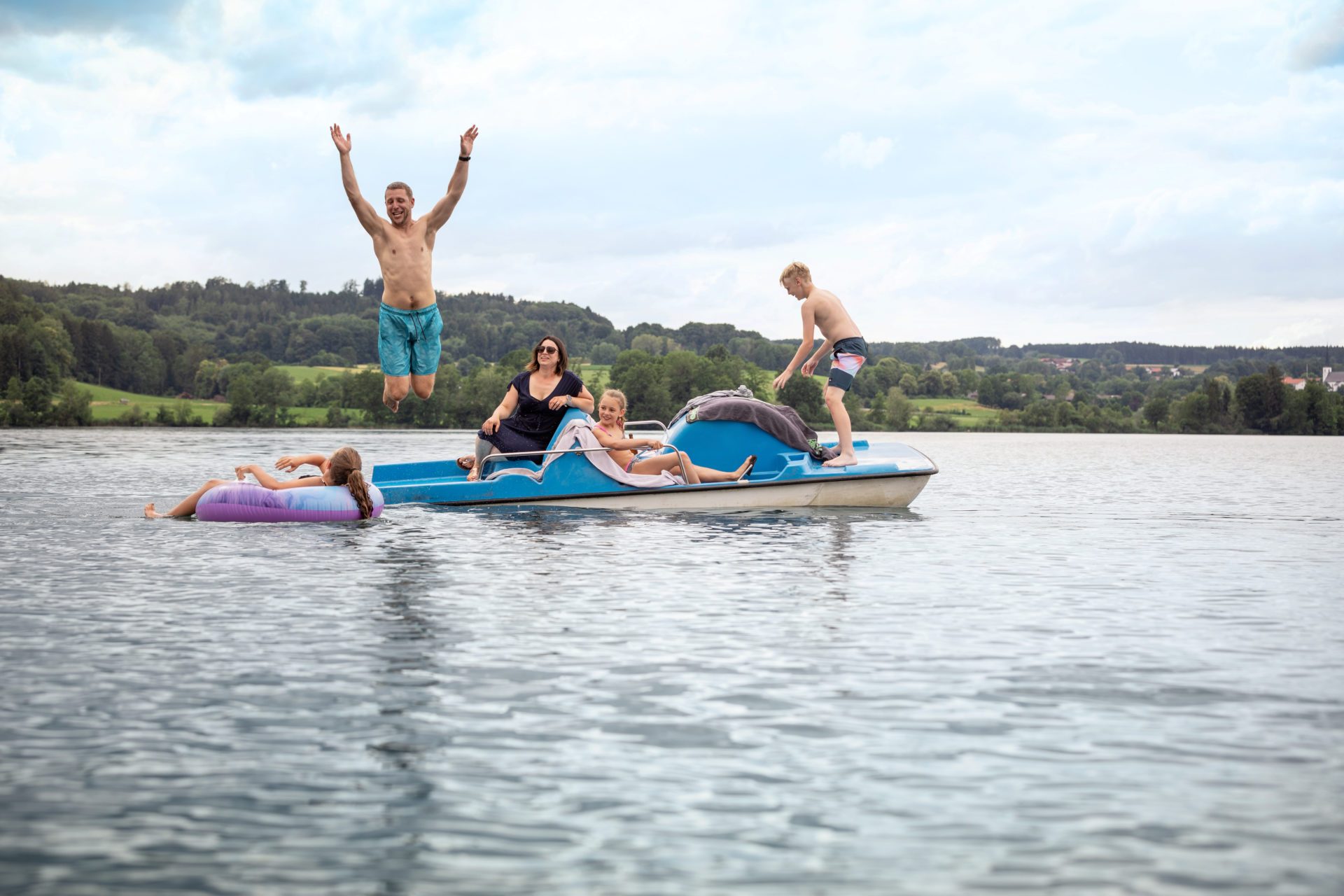 Familie auf Boot im See, einer springt ins Wasser