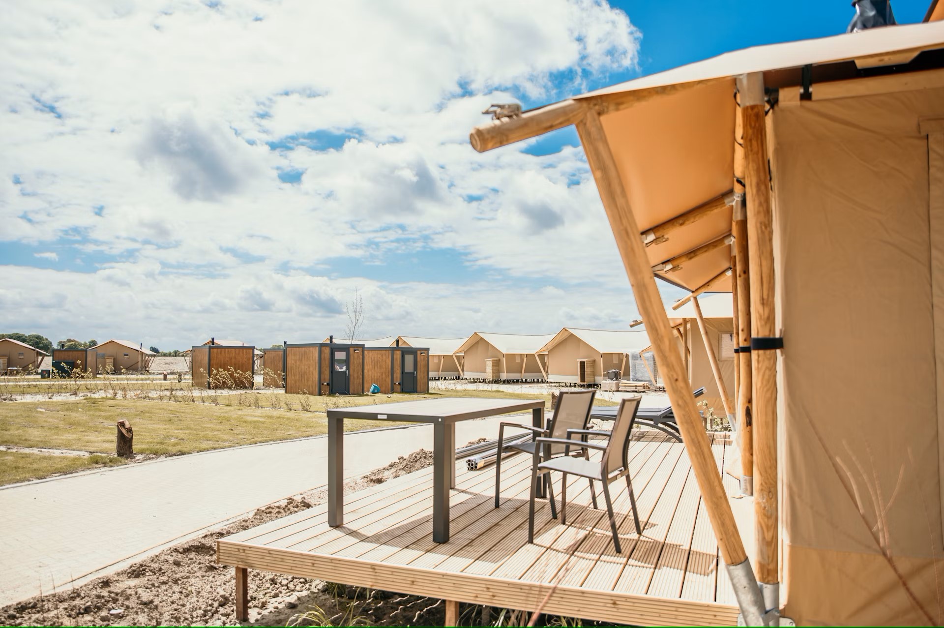 Campingplads med moderne telte og et bord på terrassen under en delvist skyet himmel.