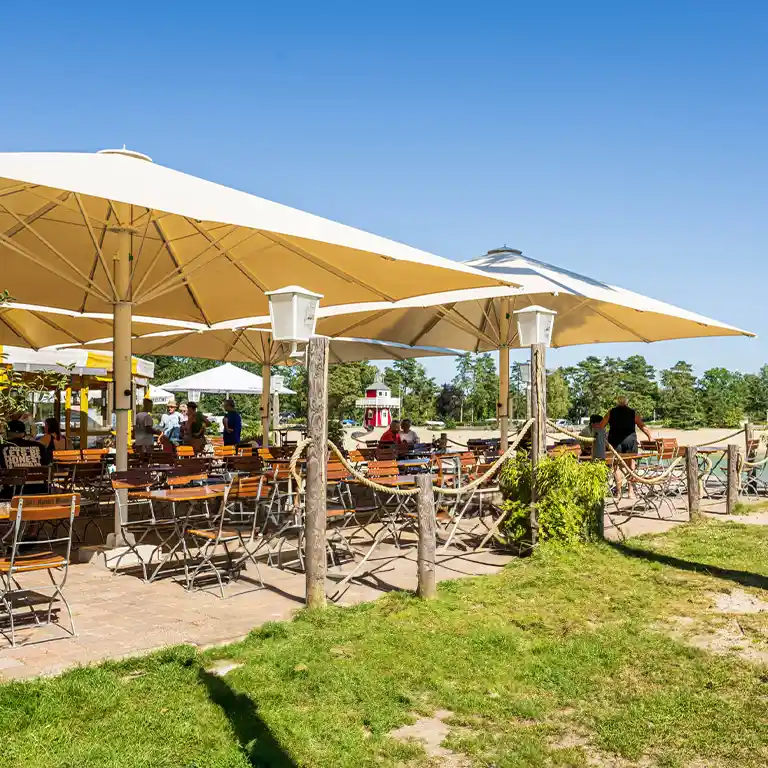 Terrasse im Südsee-Camp mit großen Sonnenschirmen und Tischen.
