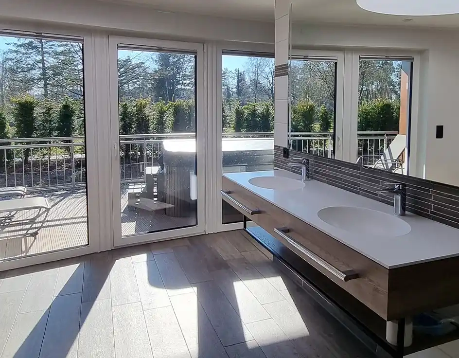 Badezimmer mit Terrasse und Blick auf den Garten, zwei Waschbecken und ein großer Spiegel.