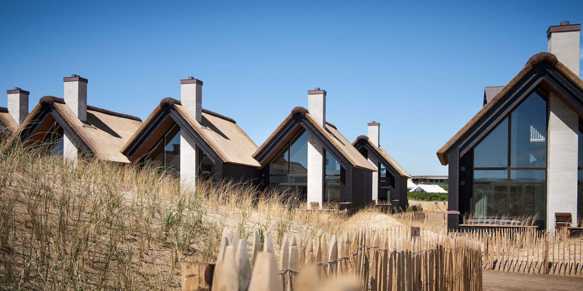 A row of modern beach houses with thatched roofs at Hvidbjerg Strand Feriepark.