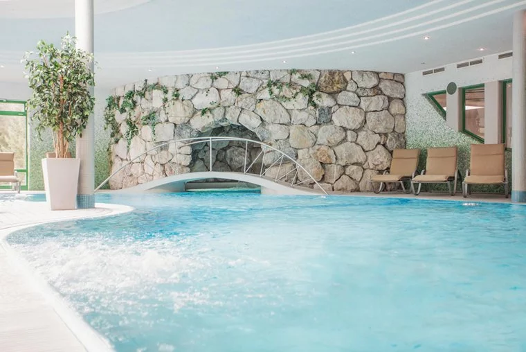 Indoor pool at Zugspitz Resort with stone wall and lounge chairs.