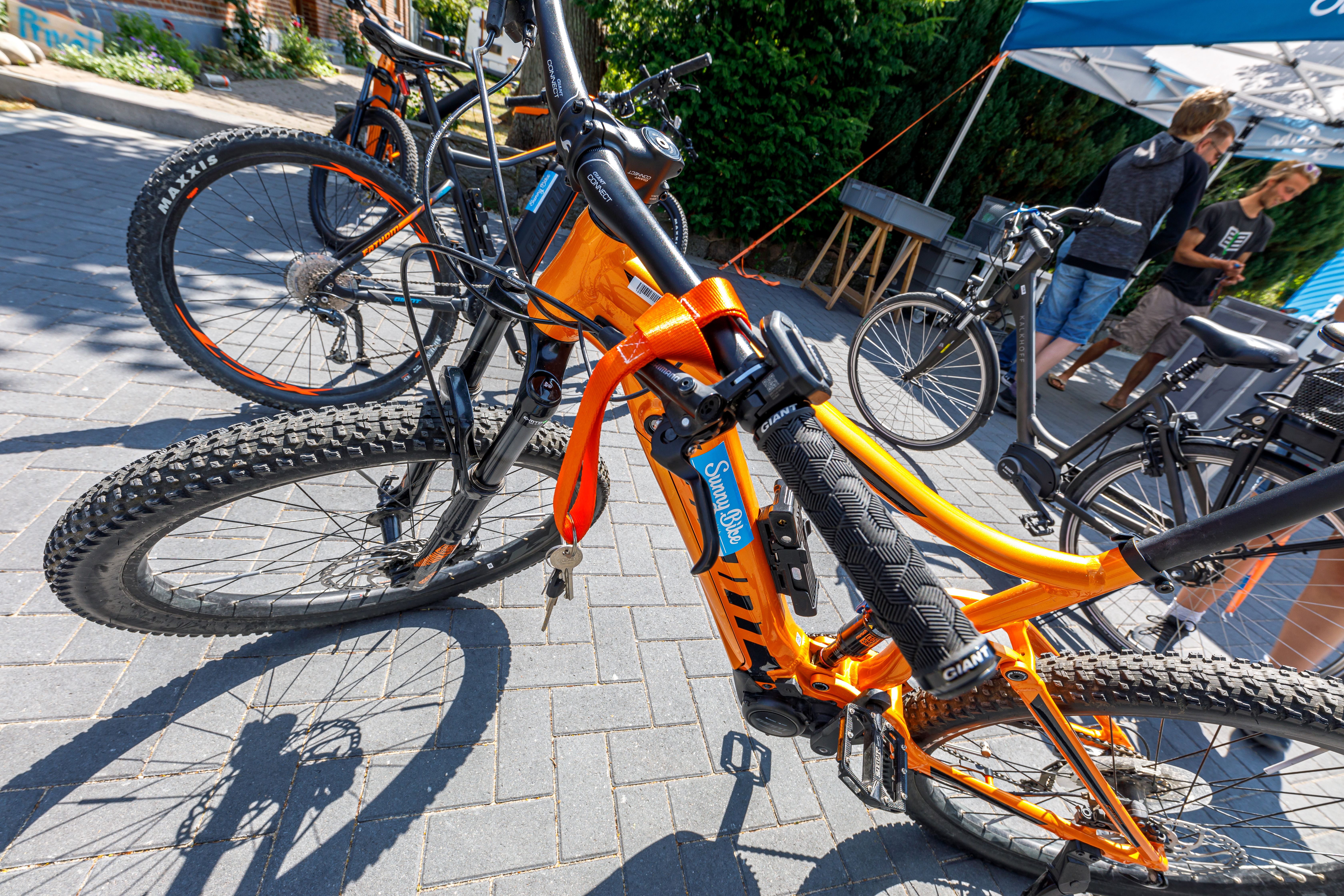 Bicicletta arancione nel campeggio con persone sullo sfondo.