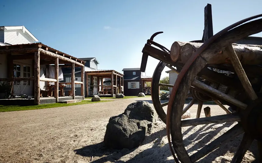 Hvidbjerg Strand Feriepark campsite with log cabin houses and a wagon wheel in the foreground.