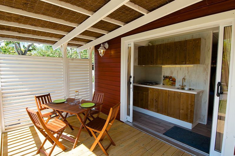 Terrasse eines Holzhäuschens im Campingplatz Nature Parc L`Ardéchois mit Tisch und Stühlen.