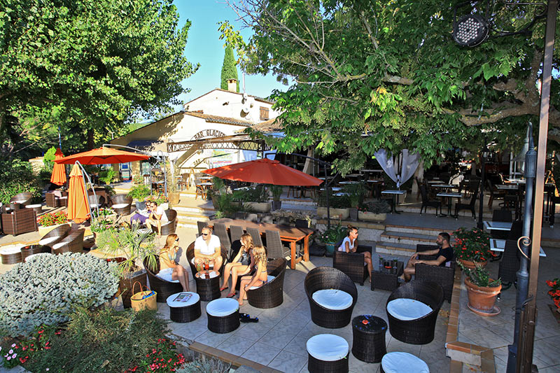 Terrasse mit Gästen unter Sonnenschirmen auf dem Campingplatz Nature Parc L`Ardéchois.