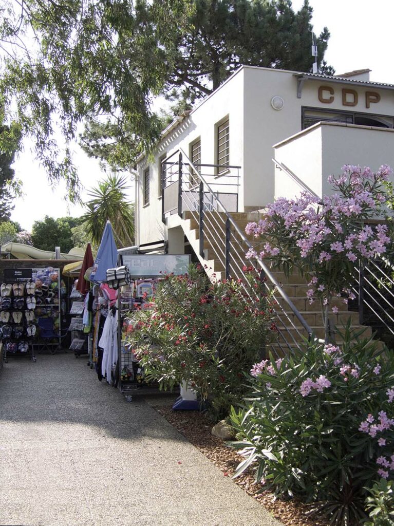 Entrance of Camping Les Criques de Porteils with a white building, stairs, and flowers.