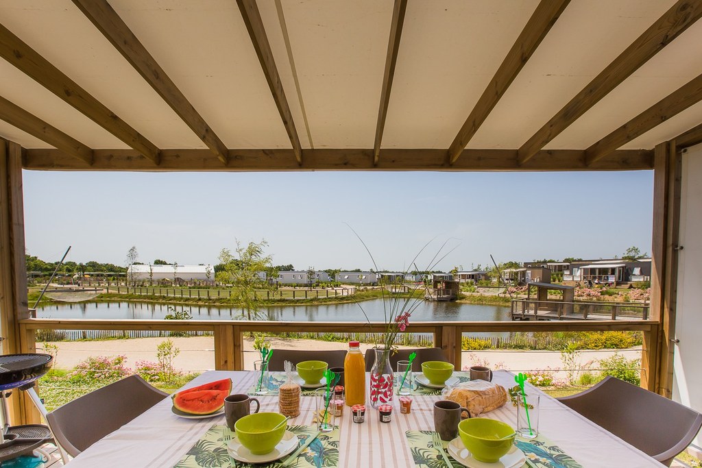 Tavolo per la colazione sulla terrazza del Camping Le Pin Parasol con vista su un lago.
